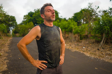 sport and fitness lifestyle portrait of young attractive sweaty and tired man exhausted after outdoors running workout on beautiful country road breathing