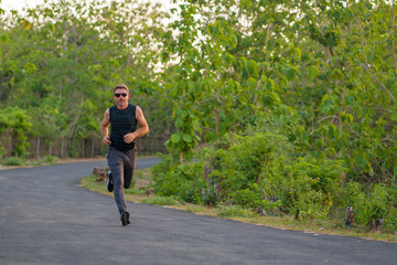 Fototapeta premium lifestyle portrait of young attractive and healthy man on his 30s or 40s running on country road doing jogging workout training happy on beautiful natural background