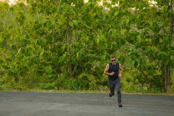 lifestyle portrait of young attractive and healthy man on his 30s or 40s running on country road doing jogging workout training happy on beautiful natural background