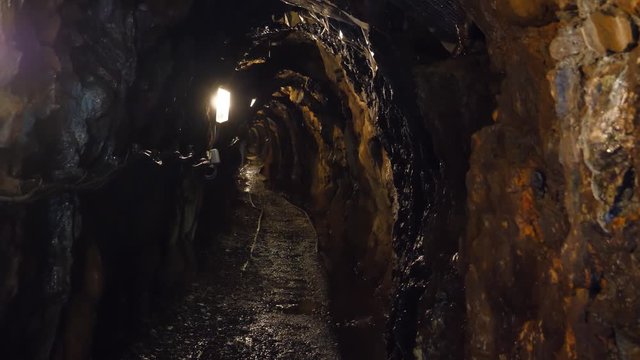 Water dripping inside of an old wet dark mine with a few electric lights and railing on the floor.