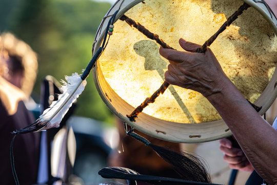 Sacred drums during spiritual singing. A traditionally constructed native drum is seen in the hands of a spiritual person with a sacred eagle feather during a park gig celebrating traditional music