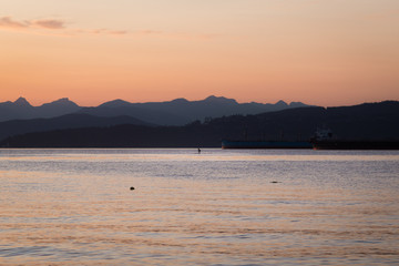 A person paddleboarding at sunset near Locarno Beach, Vancouver, Canada.
