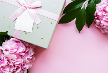 Festive background for a greeting card with a  silver gift box with a bow and flowers of  hydrangea in pink colors on a pink background