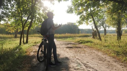 Boy in park after riding bicycle uses phone at sunset, watching social networks or chatting. Concept of healthy lifestyle in the city. - Powered by Adobe
