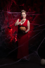 Woman in evening classic dress posing with pumpkin on black Halloween background with spider web