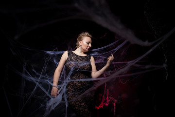 Woman in evening classic dress posing on black Halloween background with spider web