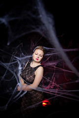 Woman in evening classic dress posing on black Halloween background with spider web
