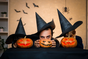 Fototapeta premium Happy family: father, brother and sister celebrate Halloween. Cheerful children in carnival costumes indoors. Cheerful children and parents play with pumpkins and black witch hats