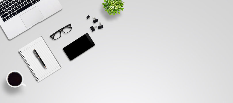Top view office desk with laptop, smartphone, pen, notebook, paper clip, glasses, flower vase, coffee, supplies, with copy space. Creative flat lay photo of workspace desk/Panoramic banner background