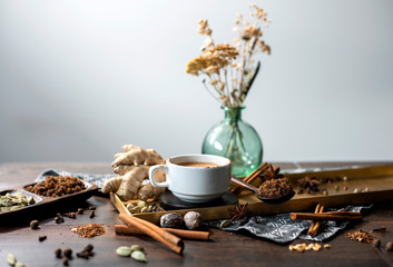 chai tea spices, chai tea latte with ginger root, cinnamon, cardamom pods, star anise, whole nutmeg, peppercorns, whole cloves on golden tray, grey cloth napkin on wooden table, copyspace, copy space