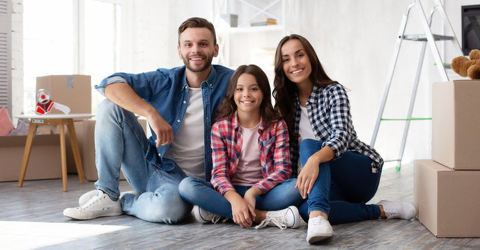 Looking forward to our bright future. Young father in denim outfit little teenage daughter and beautiful mother are sitting on the floor, hugging and smiling happily after moving house.