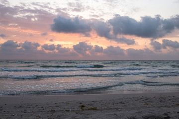 Obraz premium Dawn on the Mediterranean coast, Tunisia Sand in the foreground, small waves, the sun above the horizon, long clouds