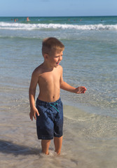 Fototapeta na wymiar A little cheerful boy enjoys summer holidays and vacations, plays, runs merrily and makes splashes on the sea on a warm summer day.