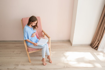 Beautiful pregnant woman reading book at home