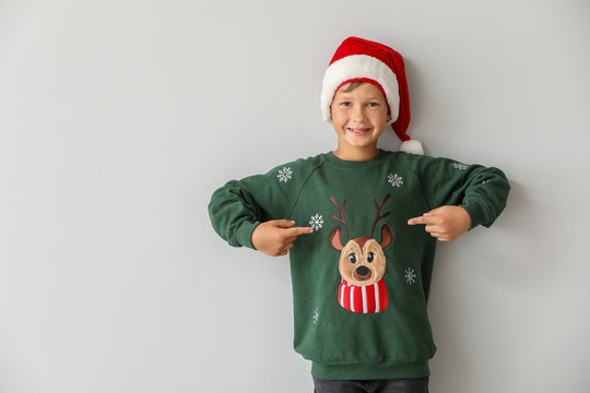 Funny boy in Christmas sweater and Santa hat on light background