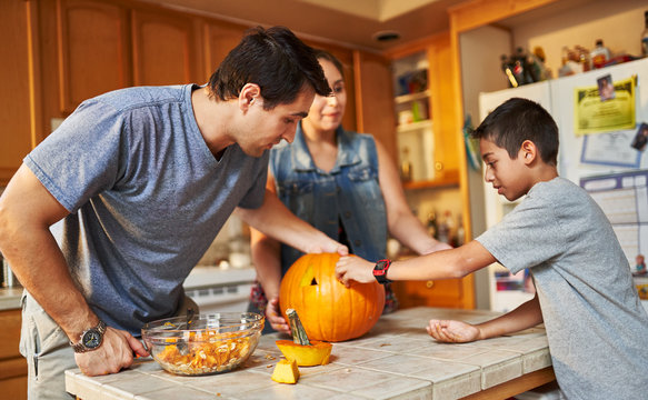hispanic american family carving pumpkin into jack o lantern at home