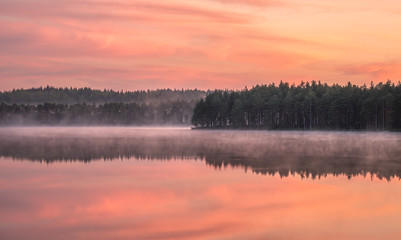 Beautiful sunrise landscape with misty mood and calm lake at foggy summer morning in Finland
