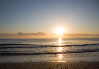 Dawn on the Mediterranean coast, Tunisia Sand in the foreground, small waves, the sun above the horizon, long clouds