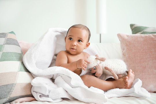 Cute African-American baby with soft towel and toy on bed at home