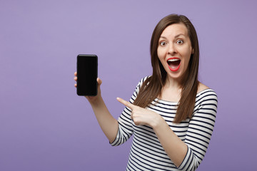 Young brunette woman in casual striped clothes posing isolated on violet purple background studio portrait. People lifestyle concept. Mock up copy space. Hold in hand cellphone with blank empty screen