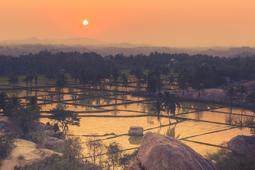 Spectacular sunset point at Hampi in Karnataka, India. Acro yoga , bouldering and music performers enjoy daily sunset here. Gymnasts outdoor hiking . Rice paddy fields at dusk