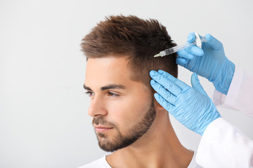 Man with hair loss problem receiving injection on grey background