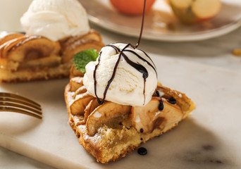 Pouring of chocolate topping onto piece of apple pie with ice cream, closeup