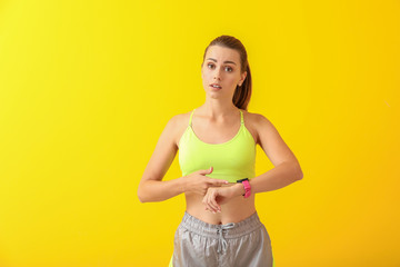 Worried young woman with watch on color background