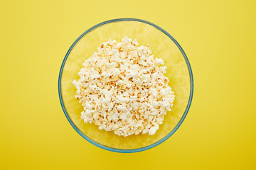 top view of delicious fresh popcorn in glass bowl on yellow background