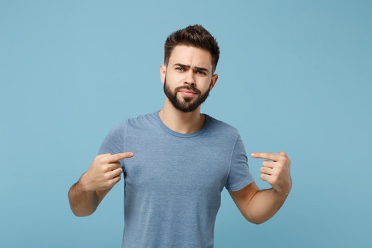 Young perplexed unconfident man in casual clothes posing isolated on blue background, studio portrait. People sincere emotions lifestyle concept. Mock up copy space. Pointing index fingers on himself.