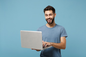 Young smiling cheerful man in casual clothes posing isolated on blue wall background, studio portrait. People lifestyle concept. Mock up copy space. Holding in hands and working on laptop pc computer.