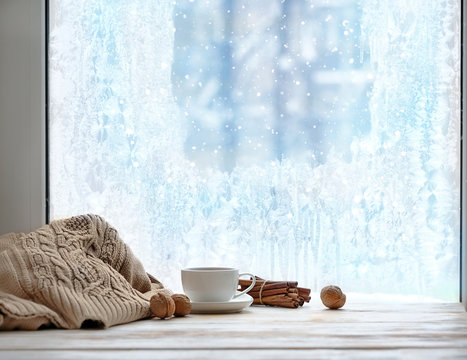 cozy winter season. cup of tea or coffee, sweater, cinnamon, nuts, frozen window. home comfort in snowy cold weather. Christmas and New Year holiday background