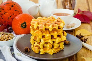 Stack of spicy pumpkin waffles on a dark plate with caramel sauce and whipped cream on a dark wooden background.  Rustic style. Fragrant autumn breakfast. Breakfast for Halloween.