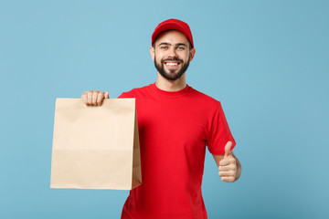 Delivery man in red uniform hold craft paper packet with food isolated on blue background, studio...