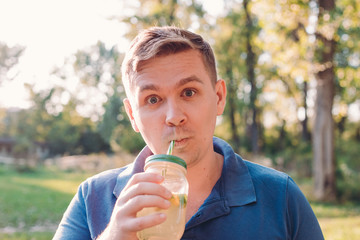 Young crazy man drinking a mojito. A man outdoors, immersed in nature, drinks a glass of homemade lemonade. Vitamins and regular life concept