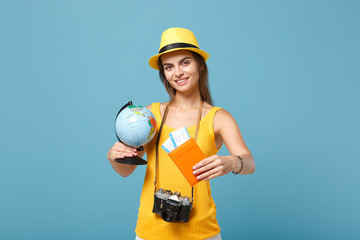 Traveler tourist woman in yellow summer casual clothes, hat hold globe tickets isolated on blue background. Female passenger traveling abroad to travel on weekends getaway. Air flight journey concept.