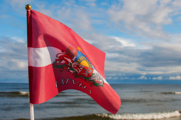 Latvia flag on a background of blue Baltic Sea and sky with clouds
