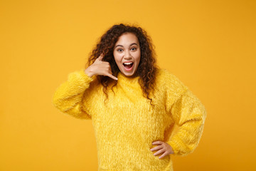 Excited young african american girl in sweater posing isolated on yellow orange background. People lifestyle concept. Mock up copy space. Keeping mouth open doing phone gesture like says call me back.