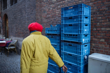 une femme marche dans la rue devant un mur de briques et des caisses bleues