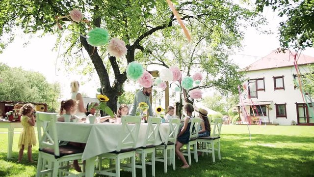 Small children sitting at the table outdoors on garden party in summer, eating.