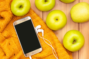 Smart phone with headphones, soft knitted yellow plaid and apples. Autumn music concept. Copy space on screen mobile device