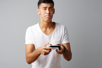Young teen man playing with console joystick over a gray background