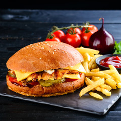 Burgers with juicy cutlet, fresh vegetables, crispy bun with sesame seeds on a wooden table. Traditional fast food.