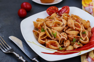 Conchiglie Italian pasta shells with cherry tomatoes and tomato sauce on dark background, horizontal orientation, closeup