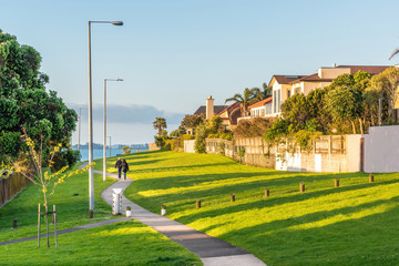 View of people walking away on concrete pathway in leafy Auckland suburb towards sea