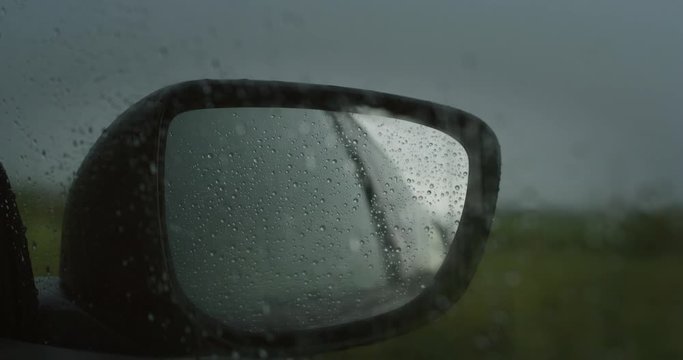 Slow motion close up of retrovisor mirror with water drops during a rain.