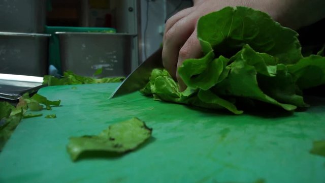 Close up footage of cook cutting lettuce on green teflon board