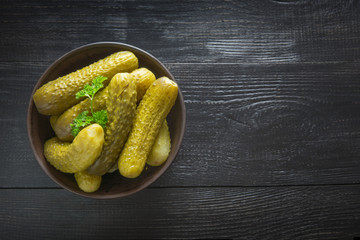 Canned vegetables cucumber in bowl on dark wooden board. Top view,
