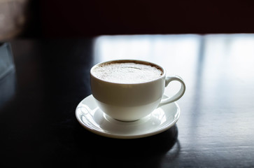 white cup with coffee on a black wooden table. The light reflected from the window is reflected on the table