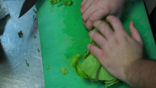 Close up footage of cook cutting lettuce on green teflon board
